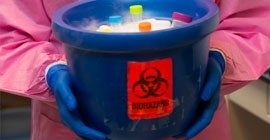 Person wearing lab coat holding a blue biohazard bucket